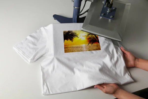 Custom t-shirt. Woman using heat press to print beautiful image of tropical seascape