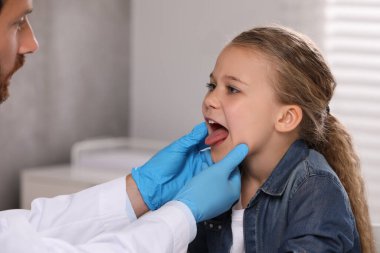 Tıbbi eldivenli doktor, kızın ağız boşluğunu içeride inceliyor.