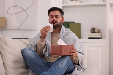 Evdeki kanepede battaniyeye sarılı hasta bir adam. Soğuk belirtileri
