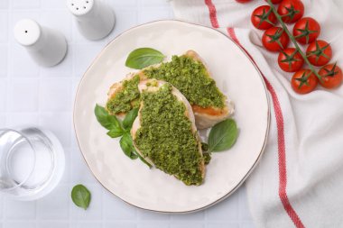 Pesto soslu leziz tavuk göğsü, domates ve beyaz fayanslı masada bir bardak su.