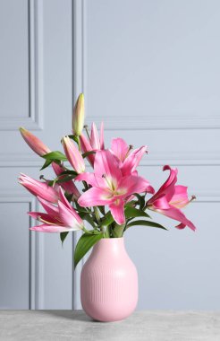 Masanın üzerinde, ışık duvarına karşı vazoda duran güzel pembe zambak çiçekleri