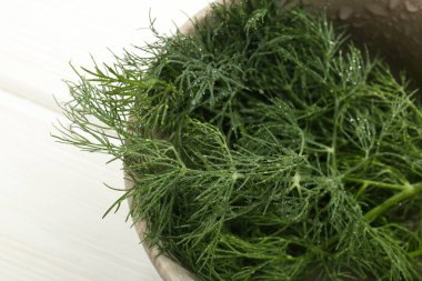 Üzerinde su damlaları olan bir kase taze yeşil dereotu beyaz ahşap masa, manzaranın üstünde.