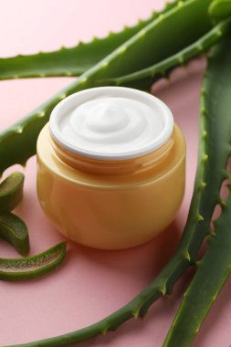 Kremalı kavanoz ve pembe arka planda aloe yaprakları, yakın plan.