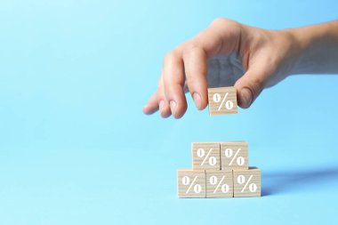 Açık mavi arka planda yüzde işareti olan küplerden piramit inşa eden kadın, yakın plan. Metin için boşluk