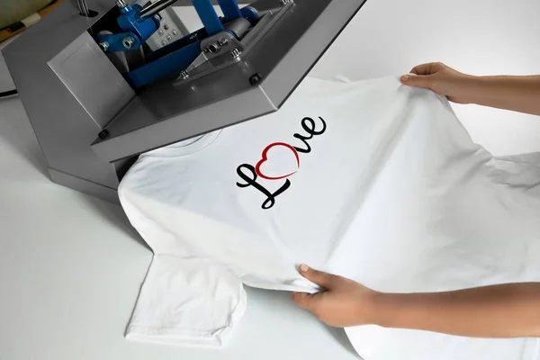 Printing logo. Woman with t-shirt using heat press at white table, closeup