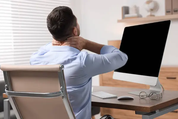 Man massaging stiff neck in office, back view