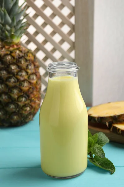 Tasty pineapple smoothie in bottle, mint and fruit on light blue wooden table