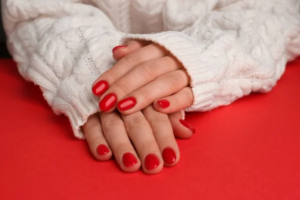 Woman with gel polish on nails at red table, closeup