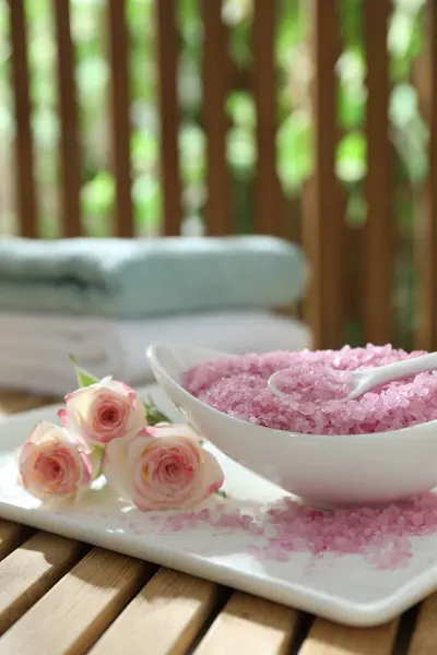 Bowl of pink sea salt and beautiful roses on wooden table, closeup. Space for text
