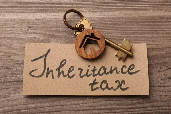 Inheritance Tax. Card and key with key chain in shape of house on wooden table, top view