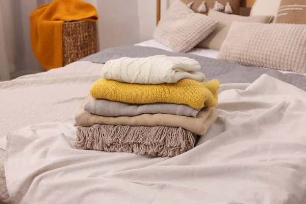 Stack of different folded blankets and clothes on bed in room. Home textile