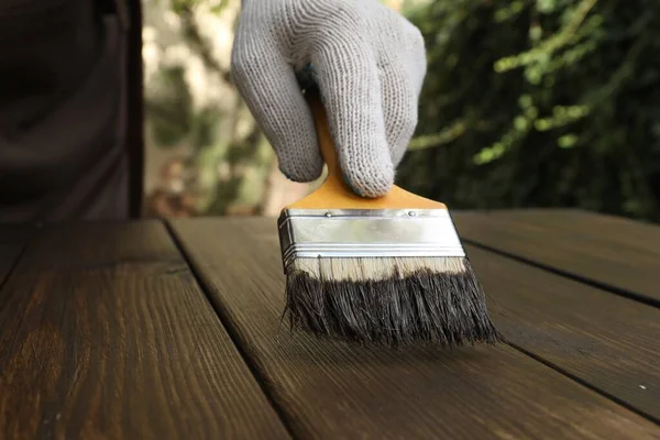 Man applying wood stain onto wooden surface outdoors, closeup