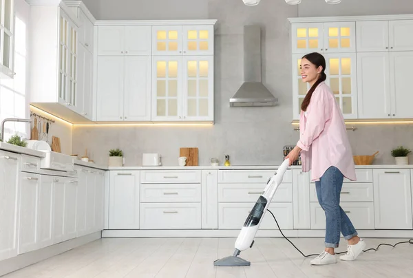 Happy woman cleaning floor with steam mop in kitchen at home. Space for text