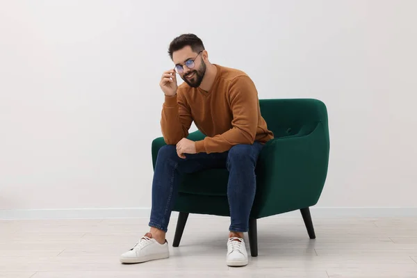 Handsome man sitting in armchair near white wall indoors