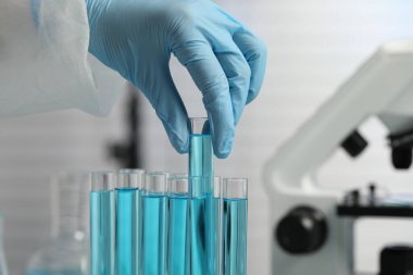Scientist taking test tube with light blue liquid in laboratory, closeup