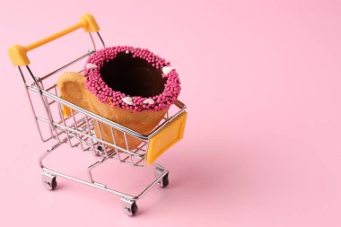 Pembe arka planda alışveriş arabasıyla süslenmiş lezzetli yenebilir bisküvi kahve fincanı. Mesaj için yer var.