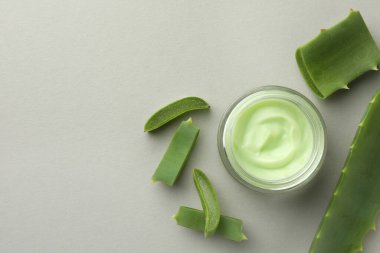 Kremalı kavanoz ve açık gri zemin üzerinde aloe yaprakları, düz yatıyordu. Metin için boşluk