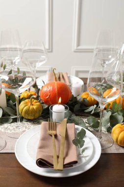 Güzel bir sonbahar sofrası. Tabaklar, çatal bıçak, gözlük, balkabağı ve çiçek dekoru.
