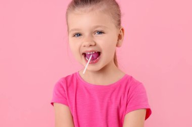 Tatlı küçük kız pembe arka planda lolipop yiyor.