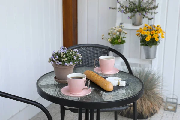 Cups of coffee, potted plant, bread and cheese on glass table. Relaxing place at outdoor terrace