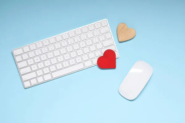 Long-distance relationship concept. Keyboard, computer mouse and decorative hearts on light blue background, flat lay