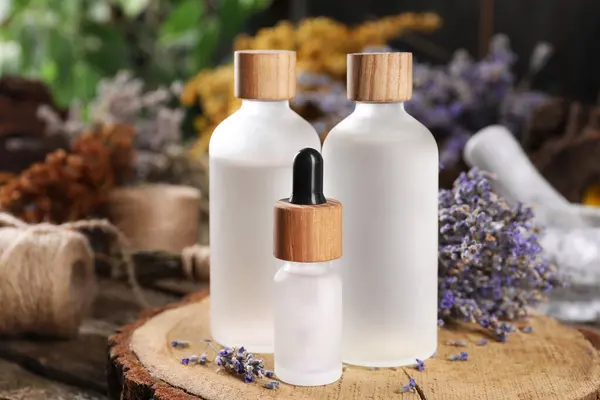 Bottles of essential oils and dry lavender flowers on wooden table, closeup. Medicinal herbs