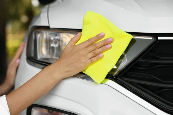 Woman cleaning car headlight with rag, closeup view