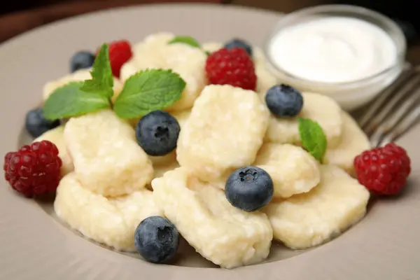 Tasty lazy dumplings with berries, sour cream and mint leaves on plate, closeup