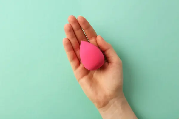 Woman with pink makeup sponge on mint color background, top view