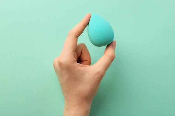 Woman with makeup sponge on mint color background, top view