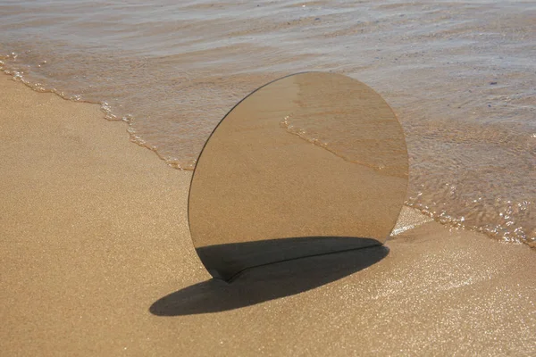 Round mirror reflecting sea on sandy beach