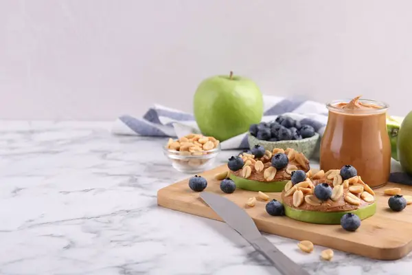 Fresh green apples with peanut butter, blueberries and nuts on white marble table, space for text