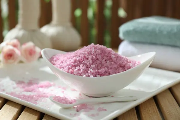 Bowl of pink sea salt on wooden table, closeup