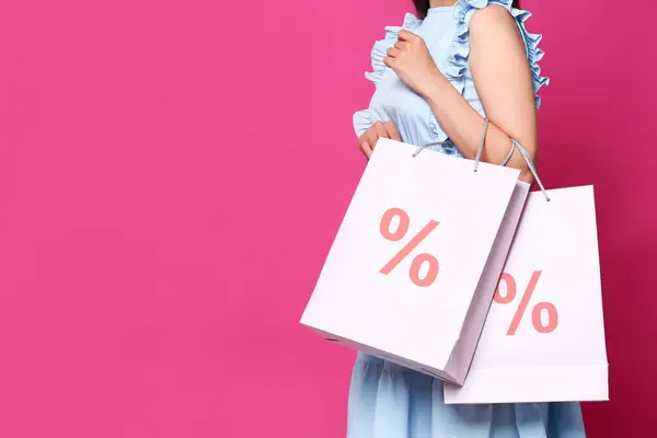Discount, sale, offer. Woman holding paper bags with percent signs against pink background, closeup. Space for text