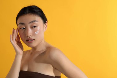 Yüzünde güneş kremi olan güzel genç bir kadın turuncu arka planda, mesaj için yer var.