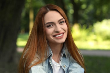 Açık havada günlük giysiler içinde mutlu genç bir kadının portresi. Çekici bir bayan gülümseyip kameraya bakıyor.