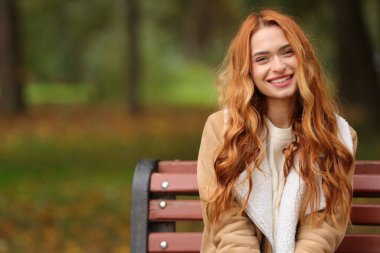 Sonbahar parkında bankta oturan gülümseyen kadının portresi. Metin için boşluk