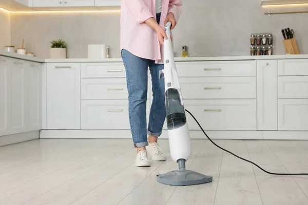 Woman cleaning floor with steam mop in kitchen at home, closeup