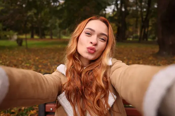 Portrait of beautiful woman taking selfie in autumn park