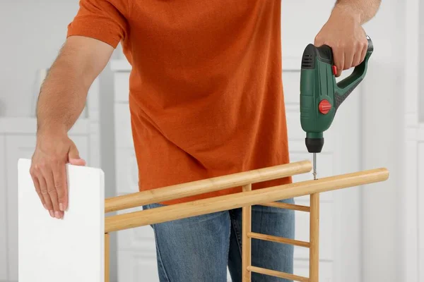 Man with electric screwdriver assembling shoe storage bench at home, closeup