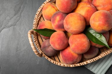 Taze şeftali ve yapraklar sepetin içinde gri desenli masa, üst manzara. Metin için boşluk