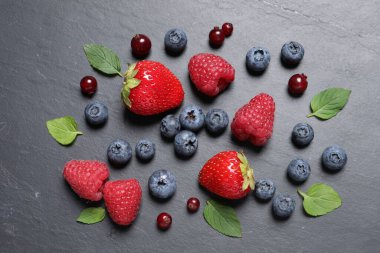 Koyu gri masada bir sürü taze olgun böğürtlen ve yeşil yapraklar vardı.