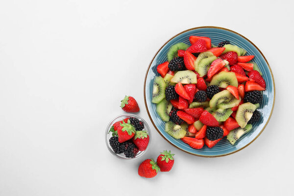 Plate of fruit salad and ingredients on light background, flat lay. Space for text