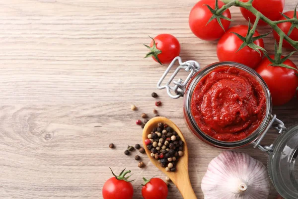 Jar of tasty tomato paste and ingredients on wooden table, flat lay. Space for text