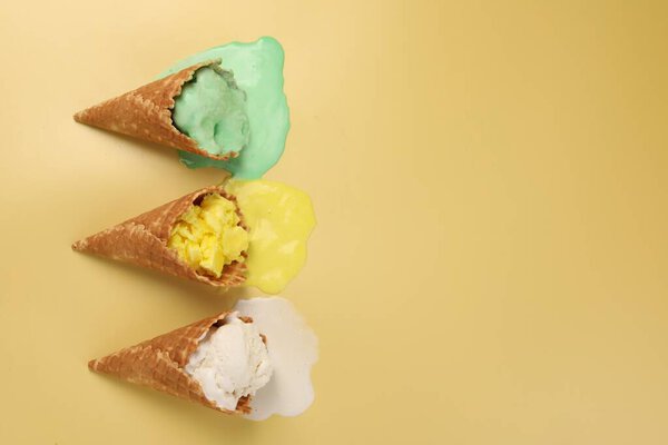 Melted ice cream in wafer cones on pale yellow background, flat lay. Space for text