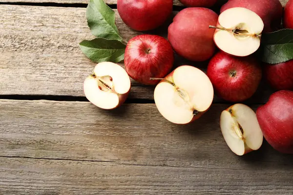 Fresh red apples and leaves on wooden table, flat lay. Space for text