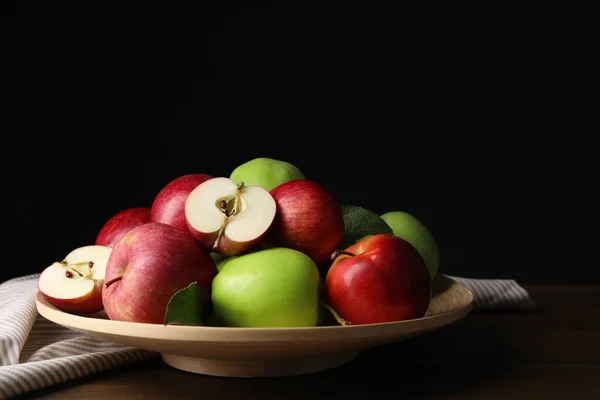 Plate with fresh ripe apples and leaves on wooden table against dark background