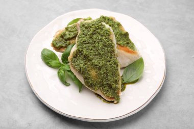 Pesto soslu leziz tavuk göğsü ve açık gri masada fesleğen, yakın plan.