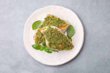 Pesto soslu leziz tavuk göğsü ve açık gri masada fesleğen.