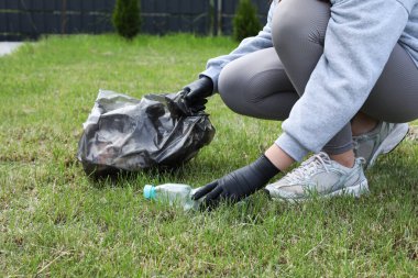 Çöp torbalı bir kadın dışarıda plastik şişe topluyor, yakın plan. Geri dönüşüm kavramı